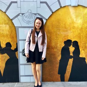 full length image of pippa standing up next to a silouette painting of alexander and eliza, on the side of the theatre