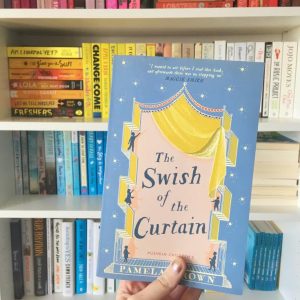 hand holding the swish of the curtain book, with rainbow bookshelves in background
