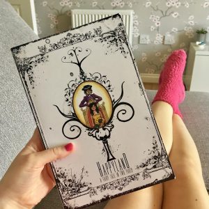 hand holding happy land book with legs and socks visible in background