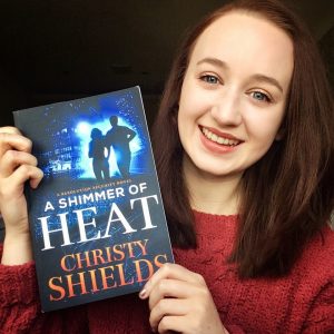 selfie of pippa wearing red jumper, holding copy of 'a shimmer of heat' book by christy shields and smiling