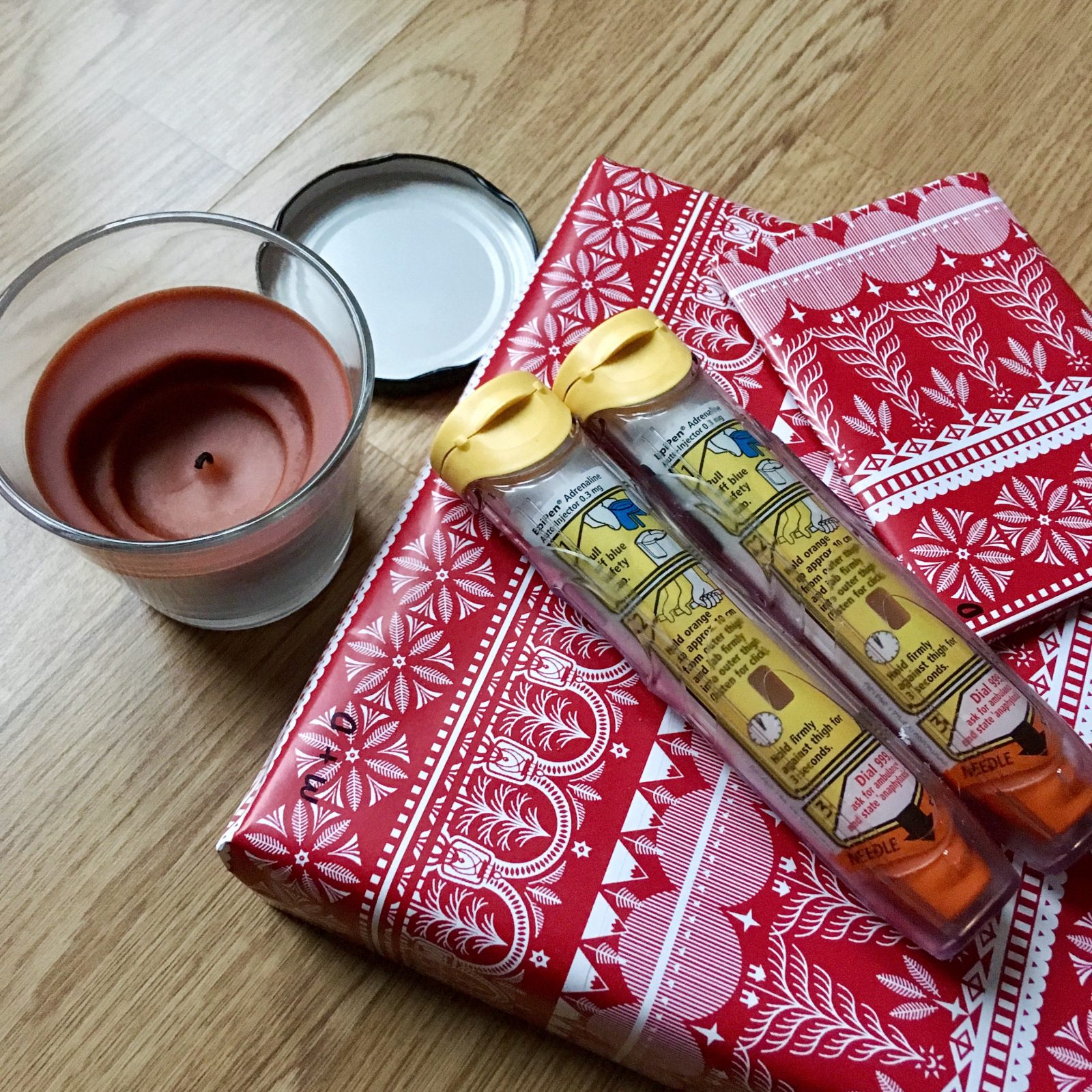 flatlay of epipens on top of presents in red wrapping paper, next to red festive candle