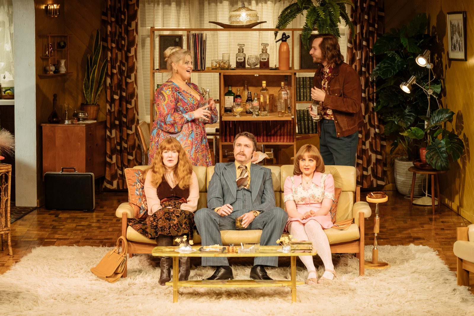 abigail's party press image featuring cast awkwardly sat on sofa and two people stood behind looking at each other suspiciously