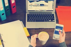 hand holding cip with laptop and phone displaying facebook in the foreground