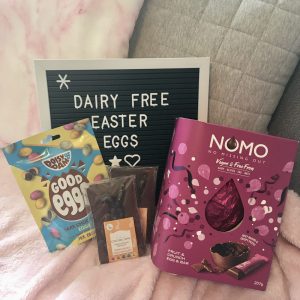 letter board reading 'dairy free easter eggs', laid on grey and pink cushions and surrounded by easter chocolate and confectionary