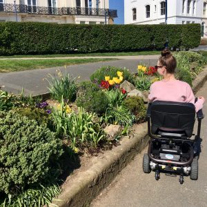 pippa in powerchair with back to camera, looking at colourful flowers along side of path