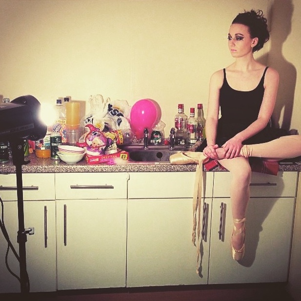 pippa at photoshoot in black ballet wear and pointe shoes with heavy make-up, sat on a counter and looking at camera taking a photo out of the shot