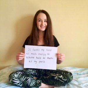 pippa sat cross legged on bed holding up sign that says 'it takes me twice as much energy to achieve half as much as my peers'
