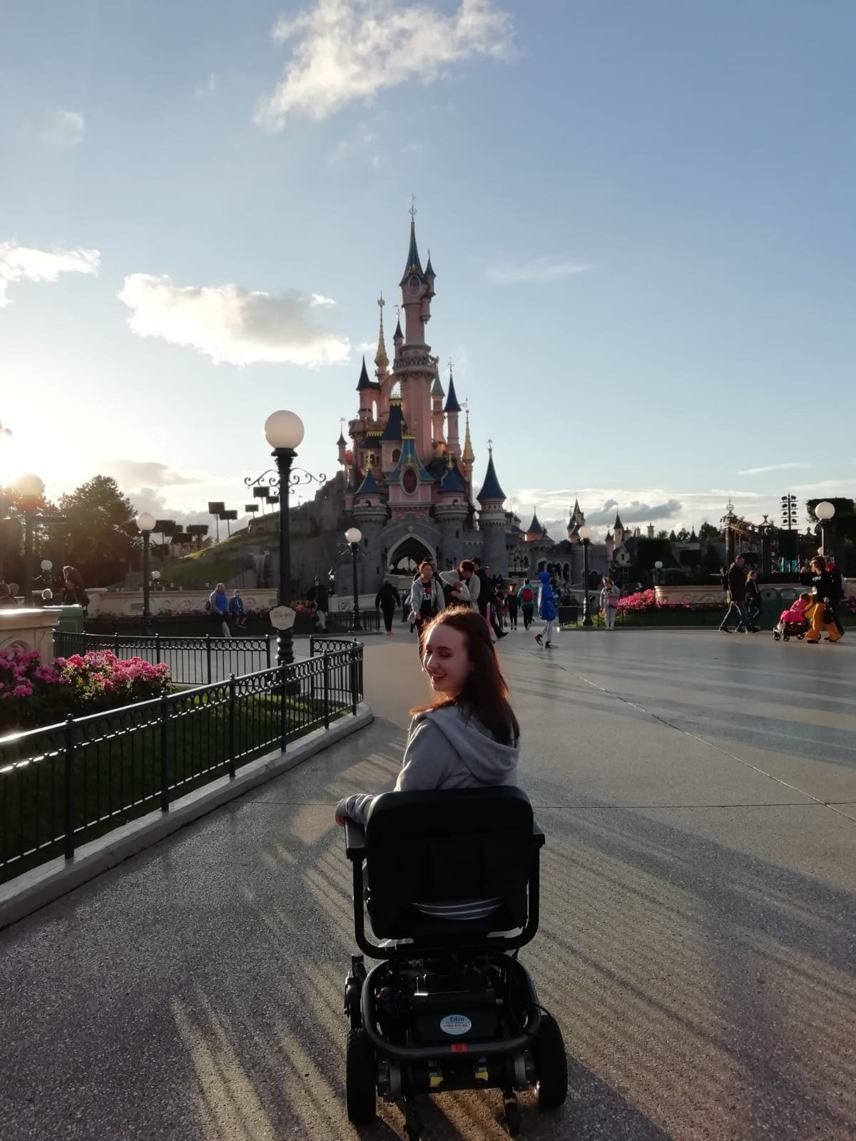 pippa in powerchair, facing disneyland castle but turning back to smile at castle