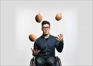 press image of aaron simmonds in wheelchair, facing front and juggling coconuts