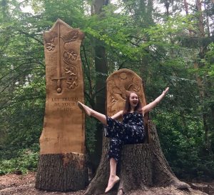 pippa posing on carved wooden chairs surrounded by forest, with arms and legs in the air and generally living her best life