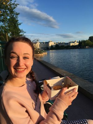 pippa sat next to lake holding up box of chicken nuggets and smiling