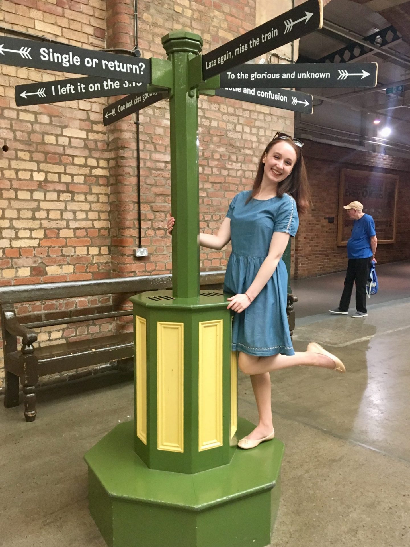 pippa shamelessly posing next to decorative signpost reading 'to the glorious and unknown', wearing a blue dress and smiling