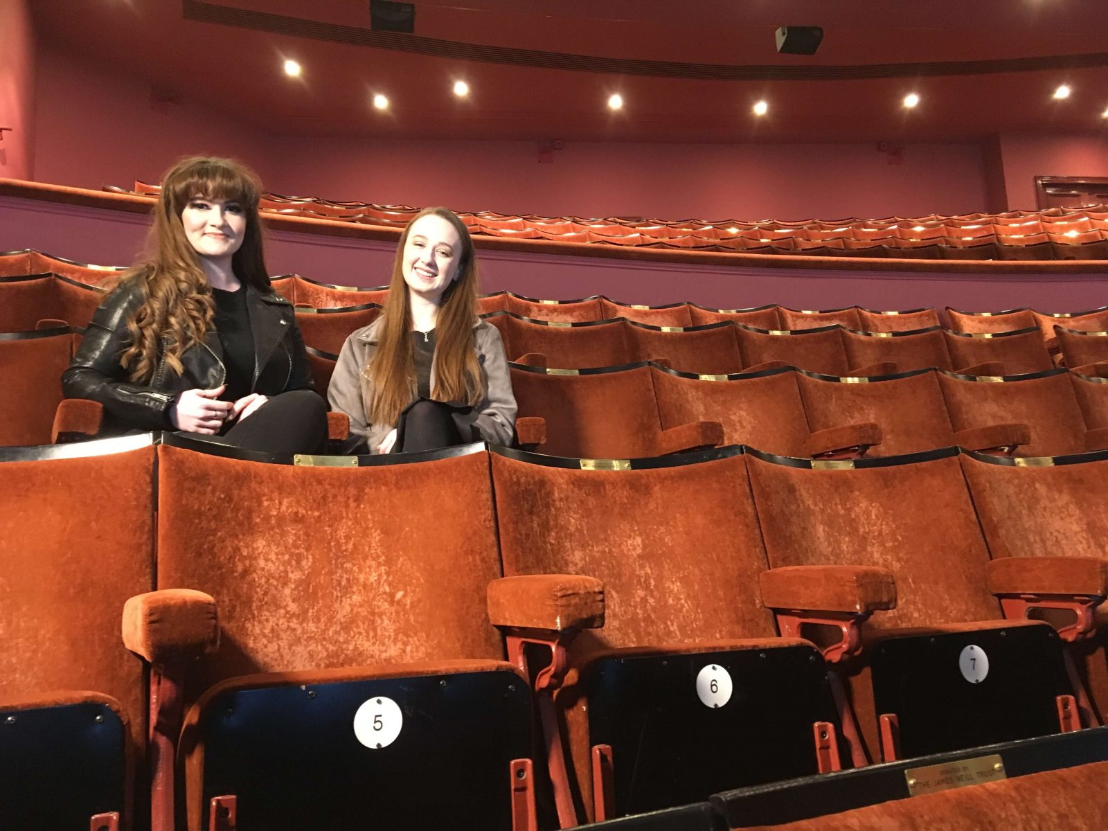 izzy and pippa sat in seats in empty theatre auditorium, facing camera and smiling 