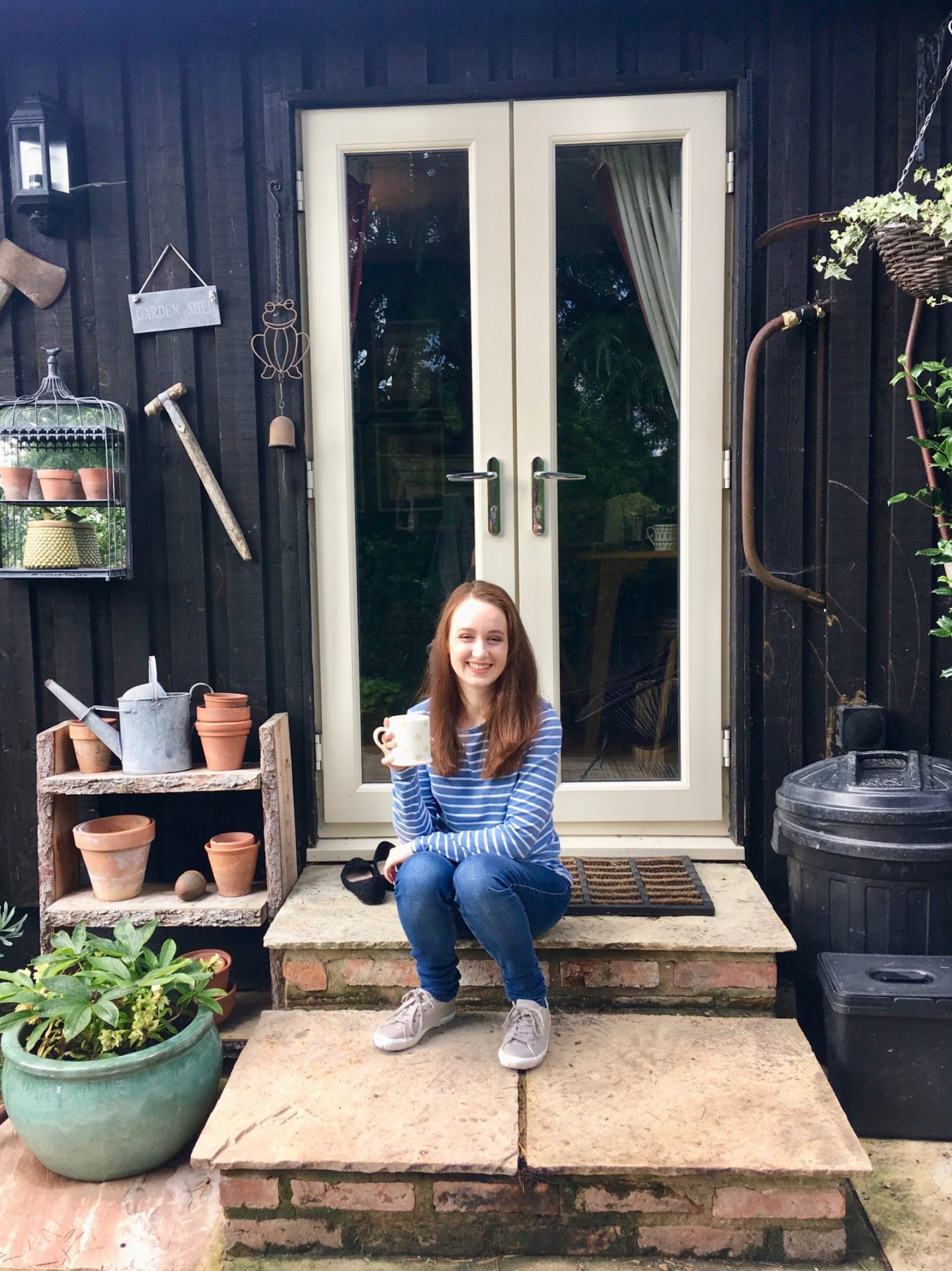 pippa sat on steps of garden shed, holding cup of tea and smiling