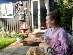 pippa in pyjamas holding tea and sat outside, looking into distance