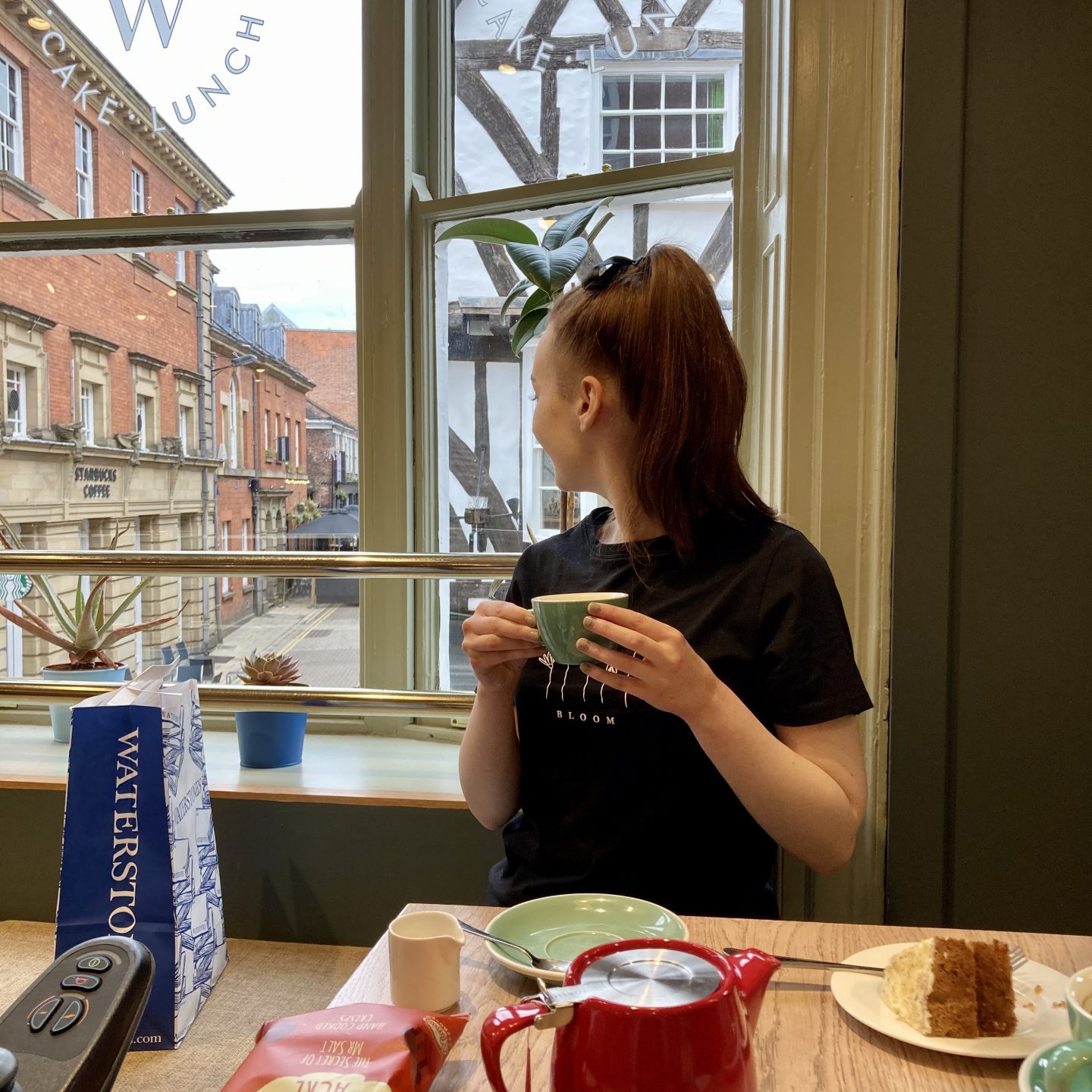 pippa sat inside cafe w, one of york's wheelchair accessible cafes, holding a cup of tea and looking out of the window behind her