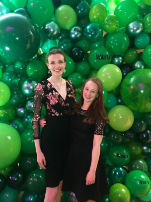 Pippa and Kate stood up in front of green balloon photo wall