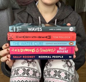 pippa in pyjamas, holding stack of books on knees with spines visible