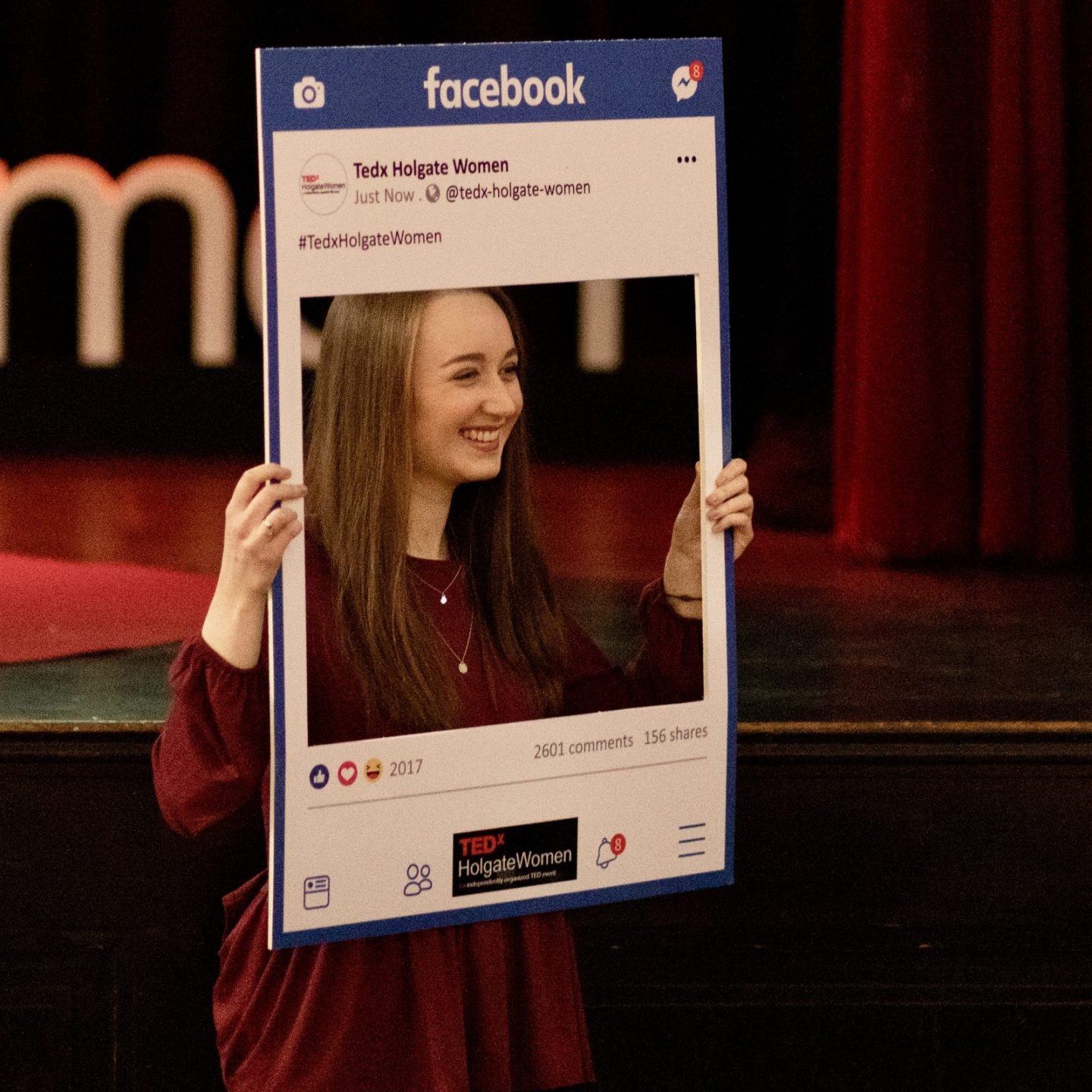 pippa stood holding up social media-style facebook photo board and smiling as somebody else takes a picture of her
