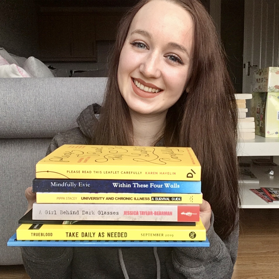 pippa holding up stack of colourful chronic-illness inspired books and smiling