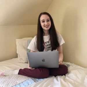 pippa sat cross legged on bed in comfy lounge clothes, laptop on knee, looking up and smiling