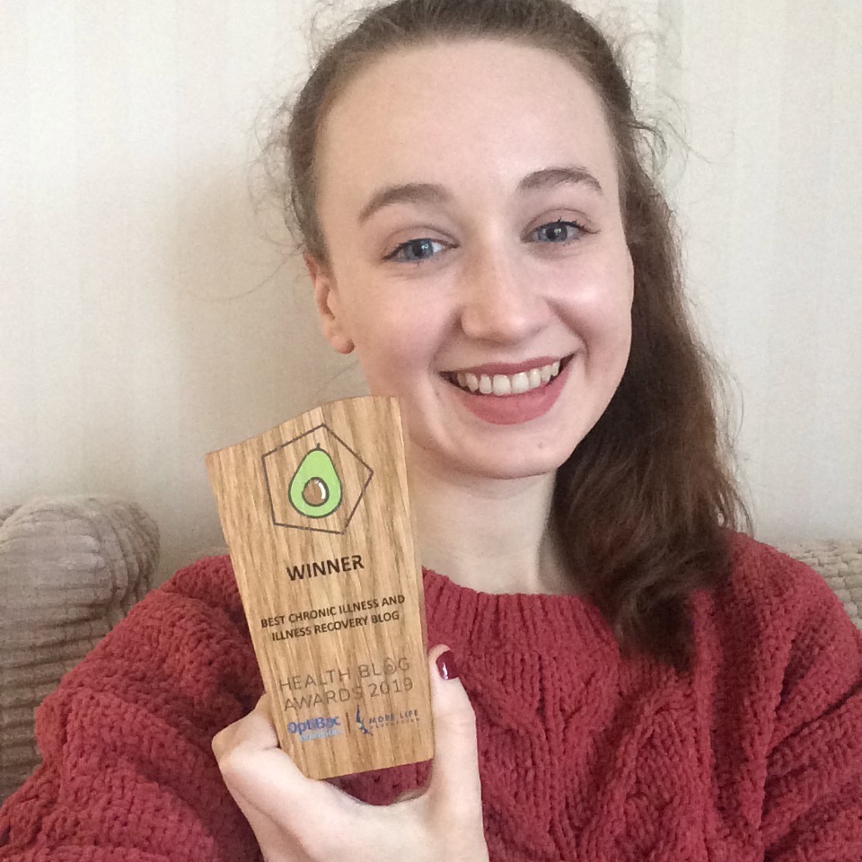 selfie of pippa in red jumper, holding up small wood "best chronic illness blog" award and smiling