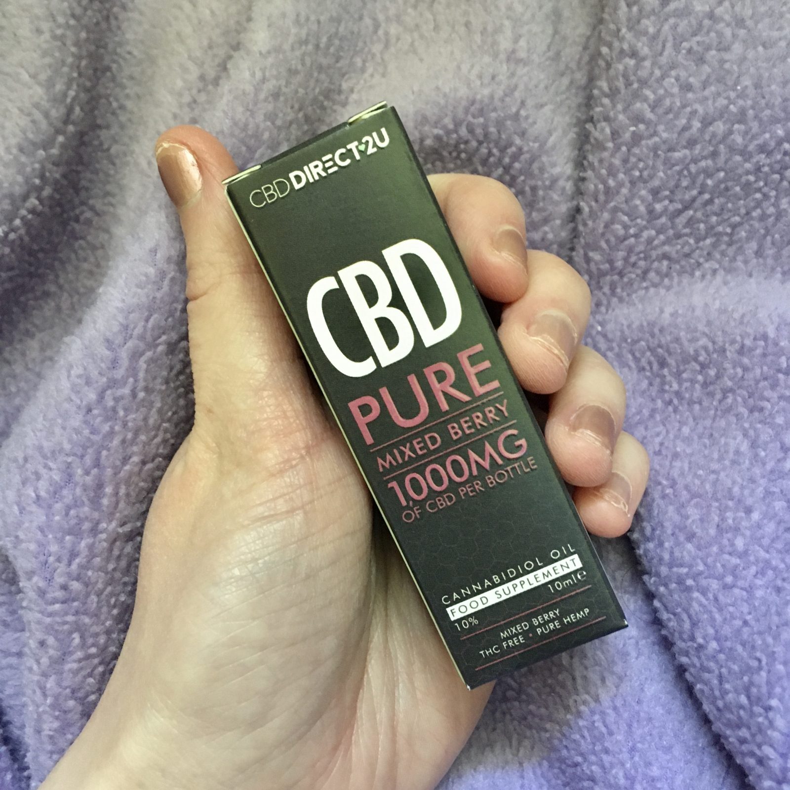 hand holding cbd in outer cardboard box packaging (black with white lettering), with purple blanket in background