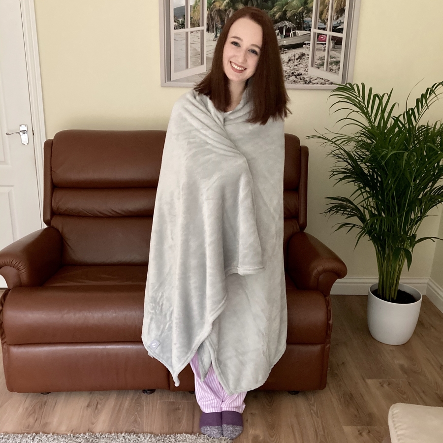pippa stood up in living room, completely wrapped up in pale grey fluffy heat holders blanket. purple heat holders sleep socks peeking out from under blanket.