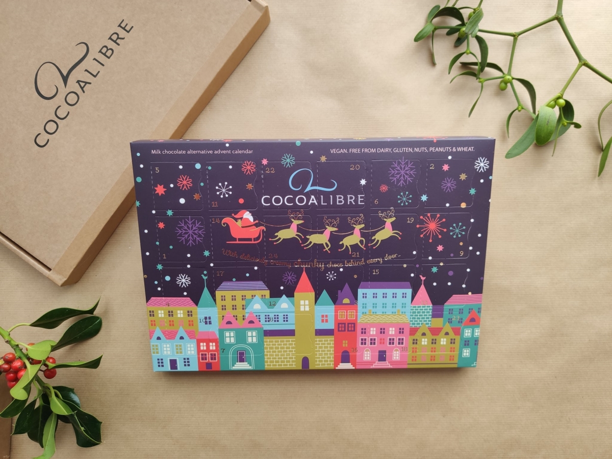 stock image of cocoa libre's advent calendar, packaged in a purple rectangular box with festive illustrations. cocoa libre branded packaging and festive leaves in background