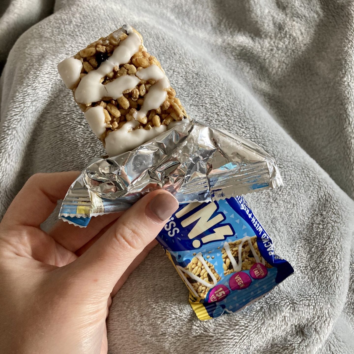 pippa's hand holding lexi's protein crispy bar, half unwrapped, showing a crunchy bar decorated with white sweet icing
