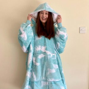 pippa stood up indoors wearing a huge green tie-dye 'oodie', a huge wearable blanket with a hood and sleeves. pippa is lifting the hood over her head and laughing