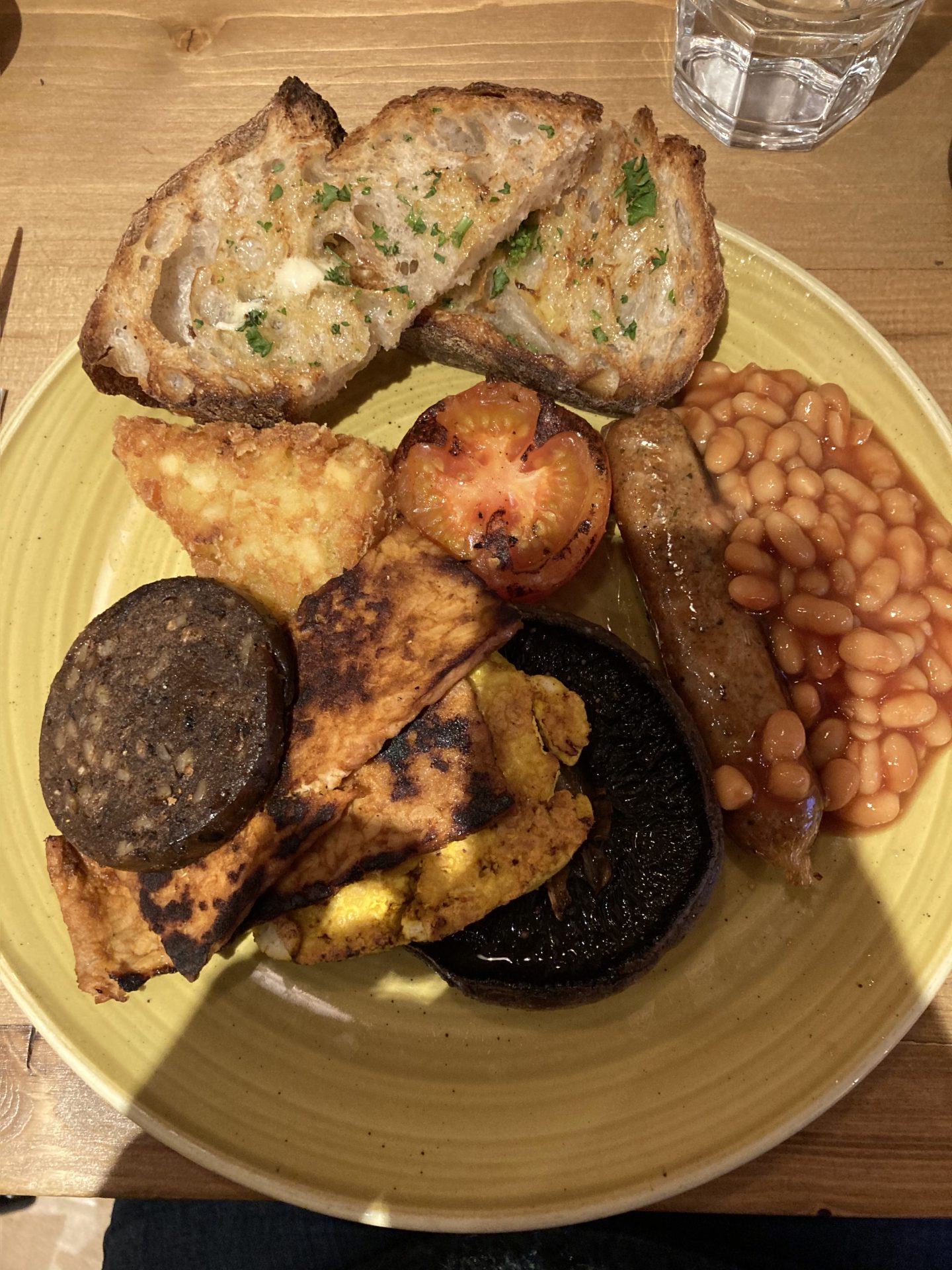 source full vegan breakfast, including grilled tempeh and tofu, beans, tomato, mushroom, hash brown, and toasted sourdough with herbs on top.