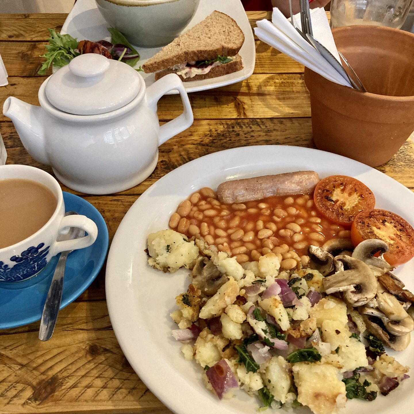 vegan full english in bruks cafe, featuring beans and bubble and squeak. cutlery in the background is stored in a cute plant pot
