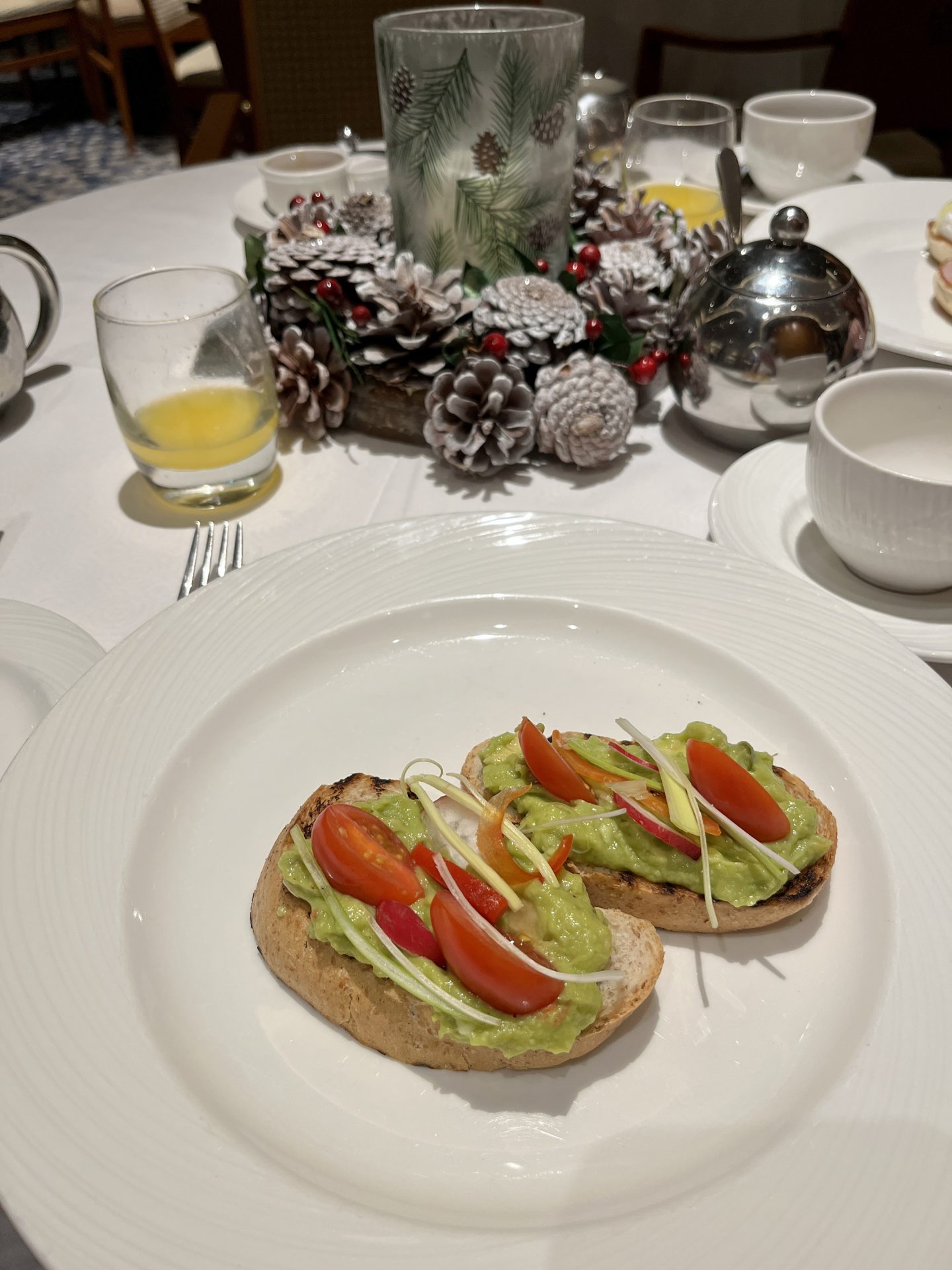allergy-friendly avocado and tomato on breakfast muffins on a table decorated for christmas, glass of orange juice in the background