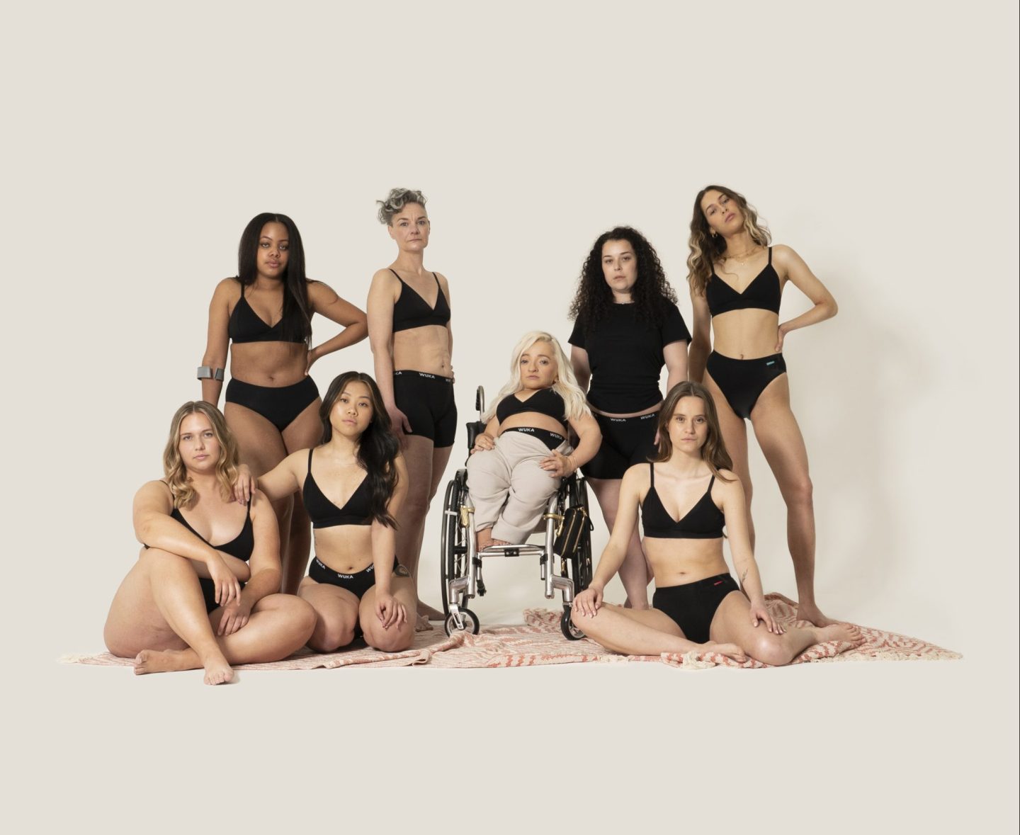 Group shot of diverse women modelling WUKA underwear. The group includes people from different ethnic backgrounds, body sizes, and visibly disabled women.