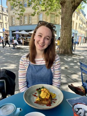 Pippa sat at an outdoor table at Boston Tea Party in Bath, with a vegan hash brown meal in front of her.