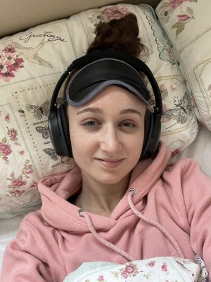 Selfie of Pippa laid down in bed, with an eyemask pushed up on her forehead and noise-cancelling headphones on.