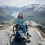 Pippa in a manual wheelchair at a viewpoint on Mount Hoven, with stunning mountains and lakes in the background.