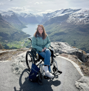 Pippa in a manual wheelchair at a viewpoint on Mount Hoven, with stunning mountains and lakes in the background.