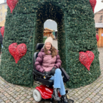 Pippa in a rented powerchair in Copenhagen, wrapped up warm in front of a huge Christmas tree at the Christmas Market.