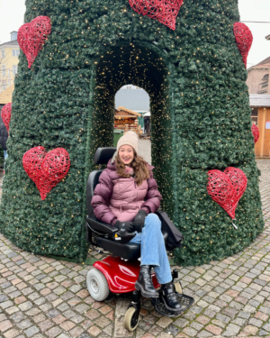 Pippa in a rented powerchair in Copenhagen, wrapped up warm in front of a huge Christmas tree at the Christmas Market.