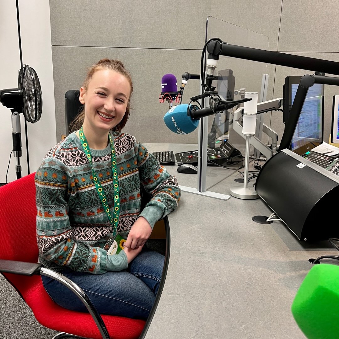 Pippa sat behind a microphone at BBC Radio Yorkshire. She's wearing a festive jumper and a sunflower lanyard, smiling as she prepares for the interview.