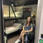Pippa, a white female wheelchair user, wearing a blue dress and in the accessible cabin on board the Night Riviera Sleeper Train.