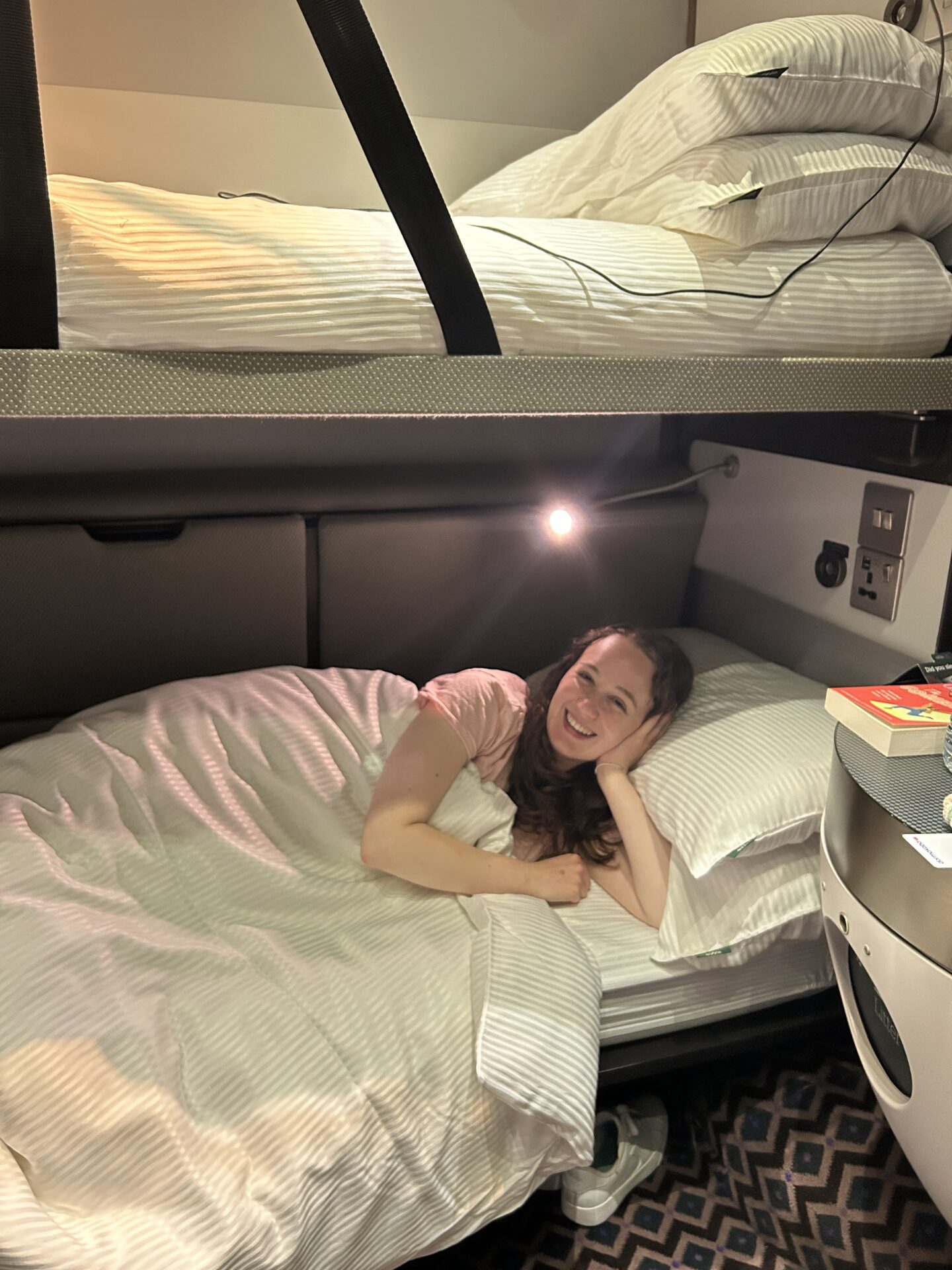 Pippa cosy in bed on the lower bunk bed on the sleeper train, with the reading light on before going to sleep.